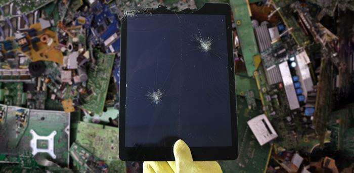 broken tablet being held above a sea of broken electronic devices as waste
