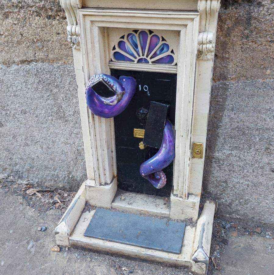 A miniature version of the door to 10 Downing Street, with purple tentacles emerging from it.