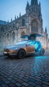 Electric Tesla Model X airport transfer car parked outside a Cambridge college chapel on a wet cobbled street