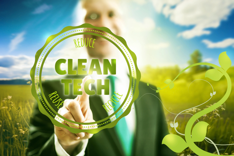 Man with blue sky and green grass behind him, pressing a Clean Tech button on the screen in front of him - promoting the green business concept.