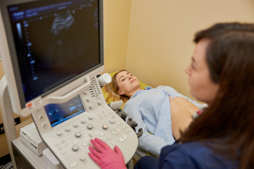 A gynecologist is performing an early pregnancy ultrasound screening, for a young female lying on a medical bed.