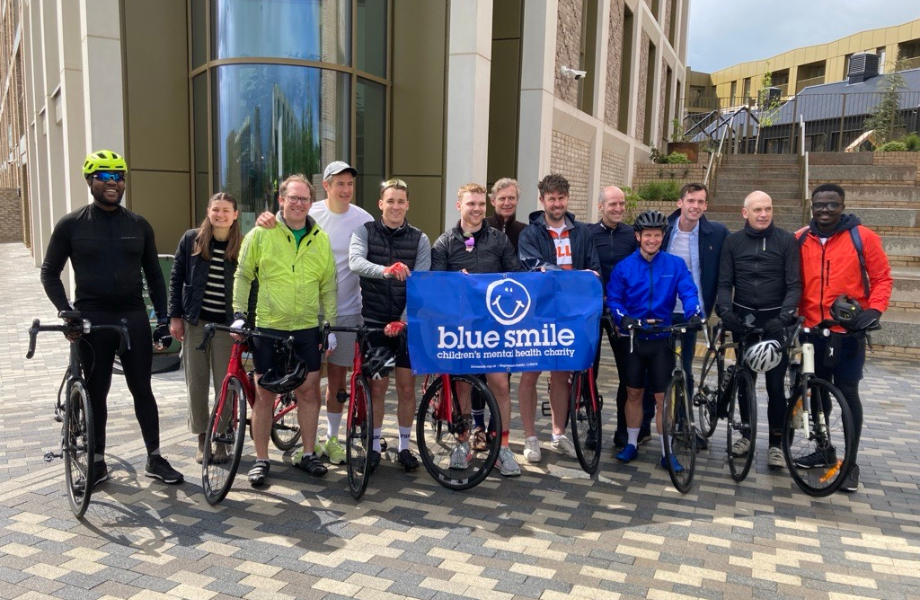 Group of people with bikes holding up a 'Blue Smile' banner outside a building