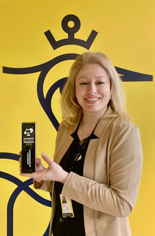 Dr Asma Rezaei holding an award in front of a yellow branded ARU background