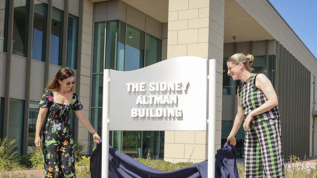 2 ladies in front of a sign the Sidney Altman Building at the Babraham Research Campus