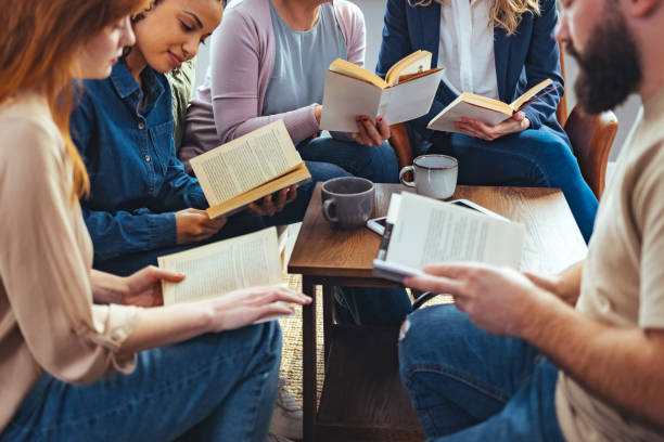 A group of people chatting and sitting around a coffee table, with open books in their hands.