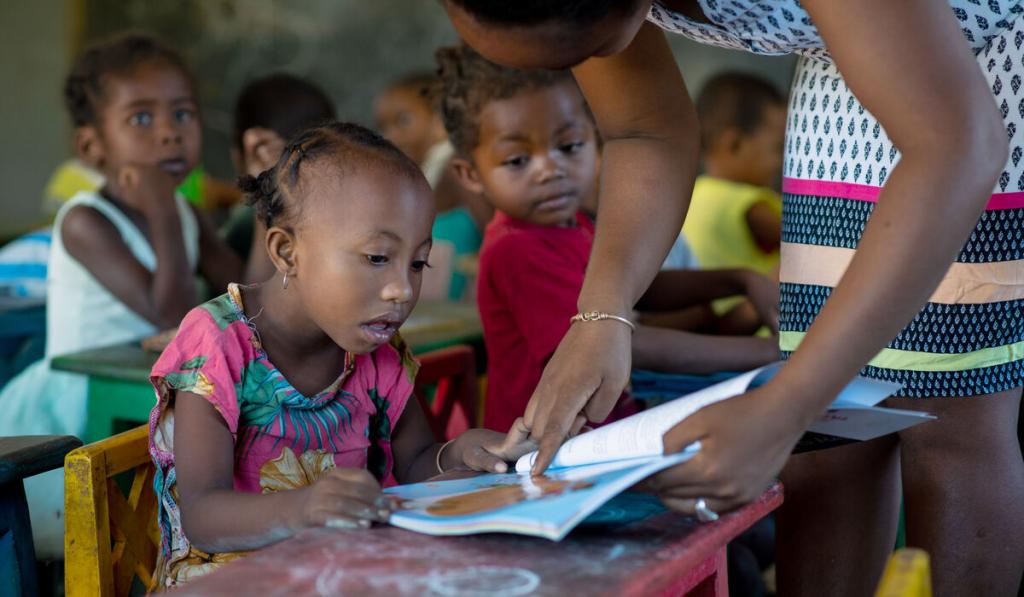 A child in Madagascar looks at a book with her teacher.