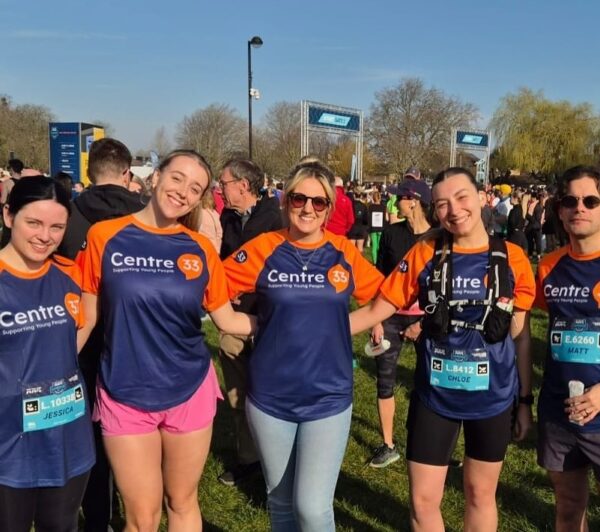 A group of five people standing together outdoors at Cambridge Half Marathon 2025 event, smiling at the camera. They are wearing matching blue and orange "Centre 33" shirts