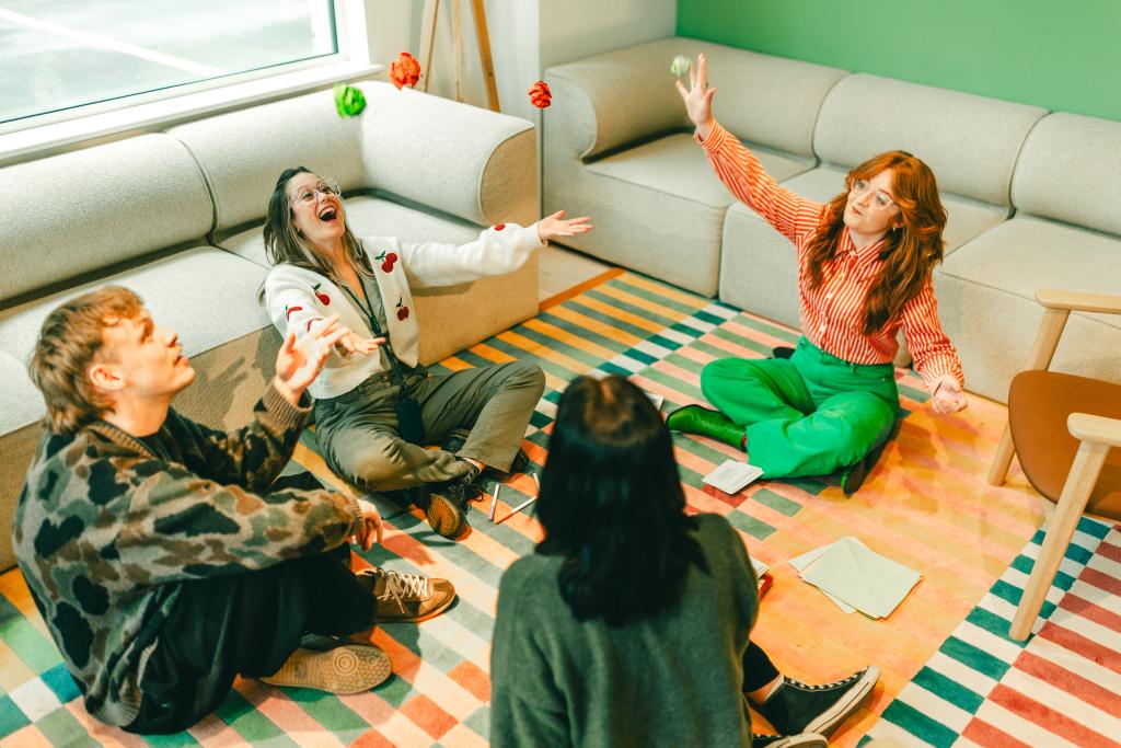 Four people sitting on a striped rug throwing scrunched up balls of paper into the air 