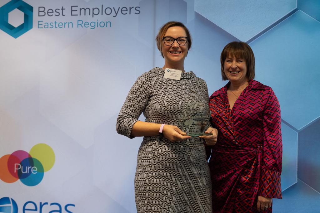 Two females holding a glass award, smiling at the camera 