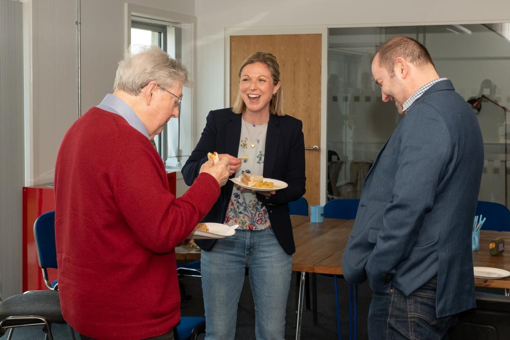A group of people at a workshop smiling and chatting to each other over some snacks.