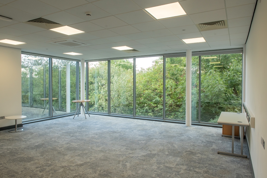 A large office with floor to ceiling windows, overlooking trees