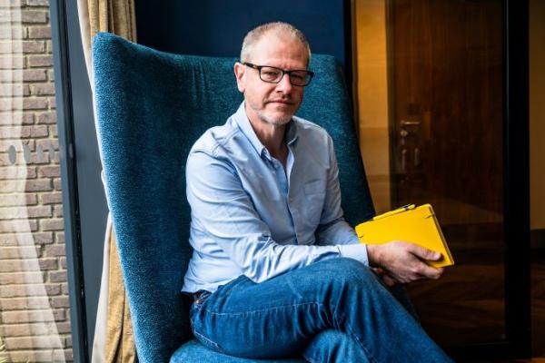 Dan Ince sitting in a blue chair with a yellow notebook 