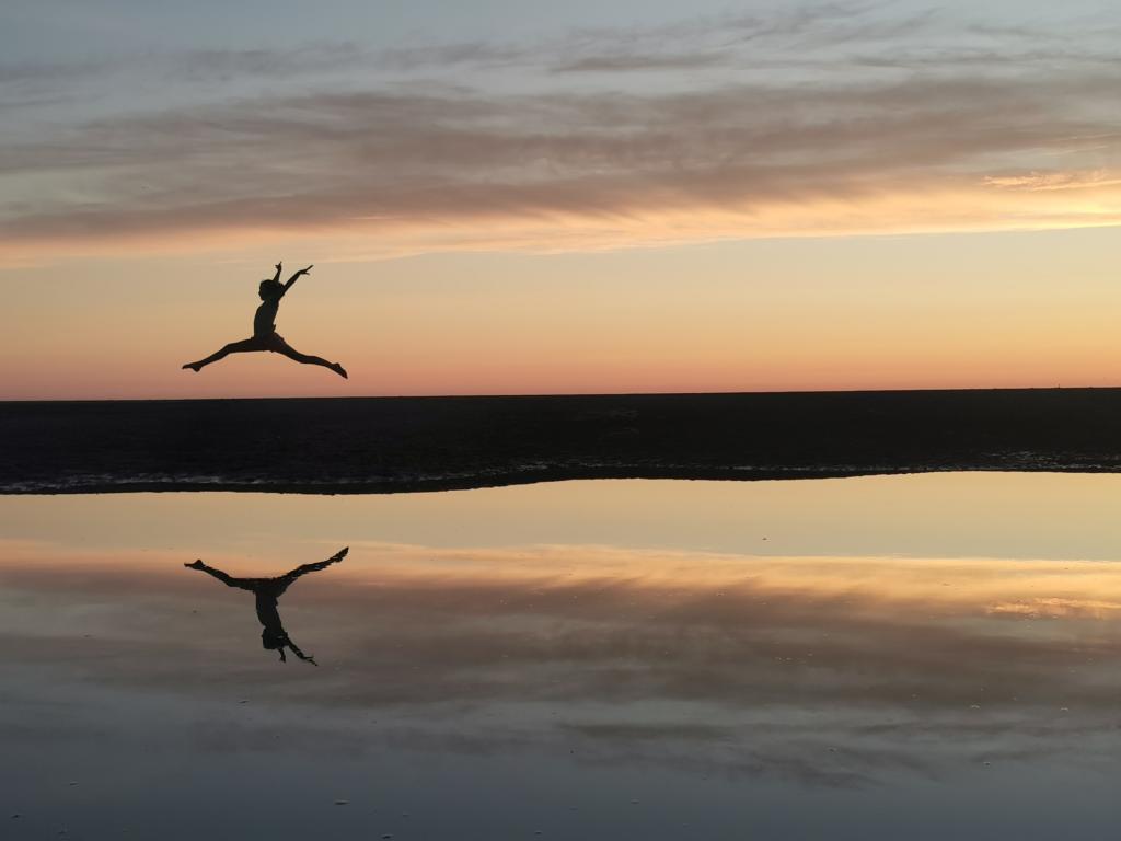 Girl leaping across the sand at sunset