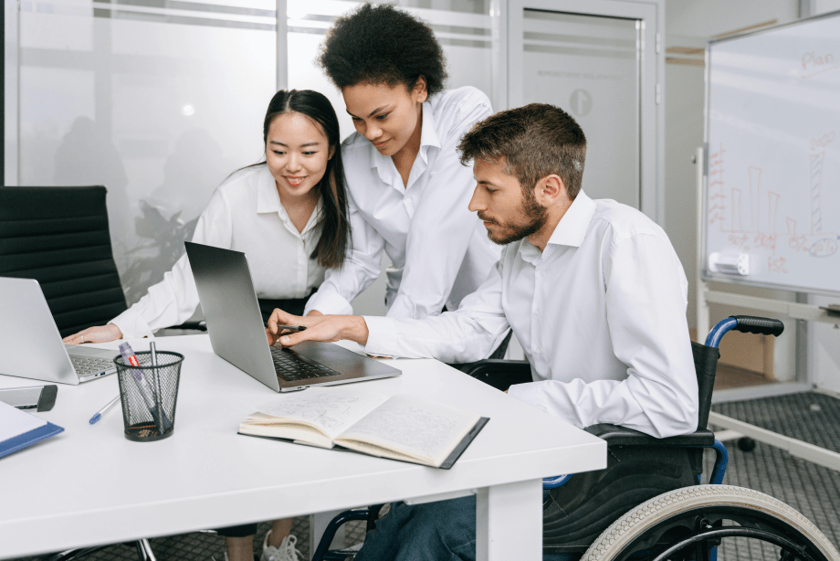 Two women and a man in a wheelchair looking at a laptop