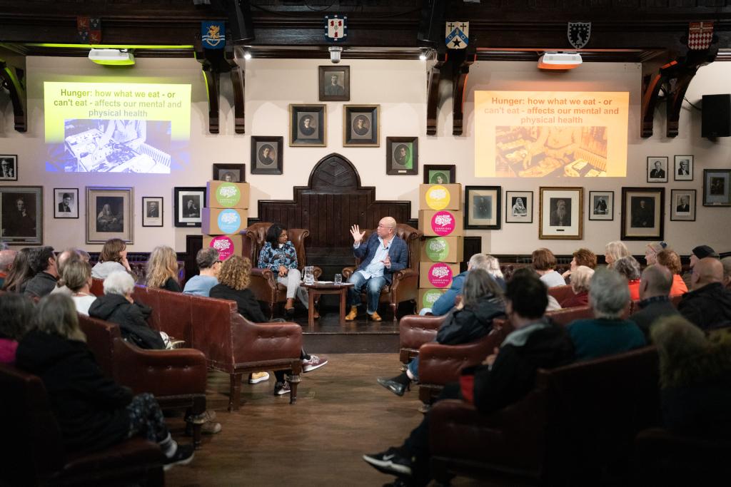 2 people talking in front of a crowed of seated people