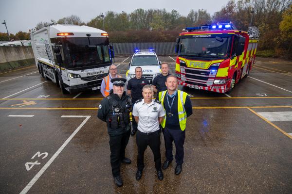 Three people stood in front of a bin lorry, police car and fire engine