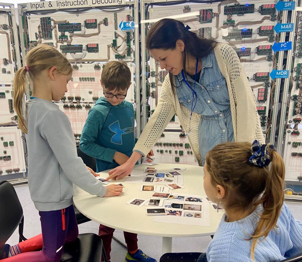 A volunteer helps a group of children create a timeline using photos of items from computing history 