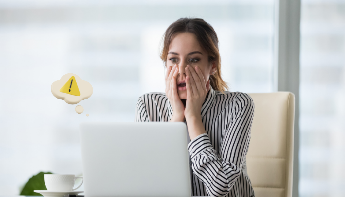 A woman looking shocked as she looks at her laptop screen implying she's made a big mistake