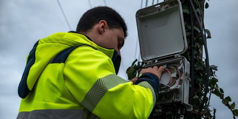 Telecom field engineer in a high-visibility jacket working on a box with cables in it