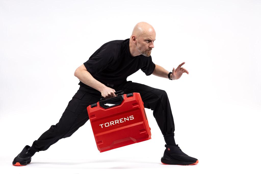 A man in black holding a red briefcase, standing in a an action pose.