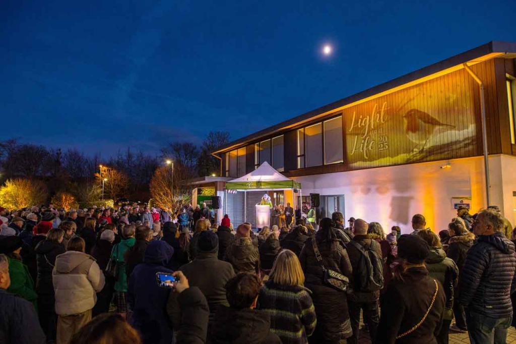 People outside looking at a picture of a Robin lit up on a building 
