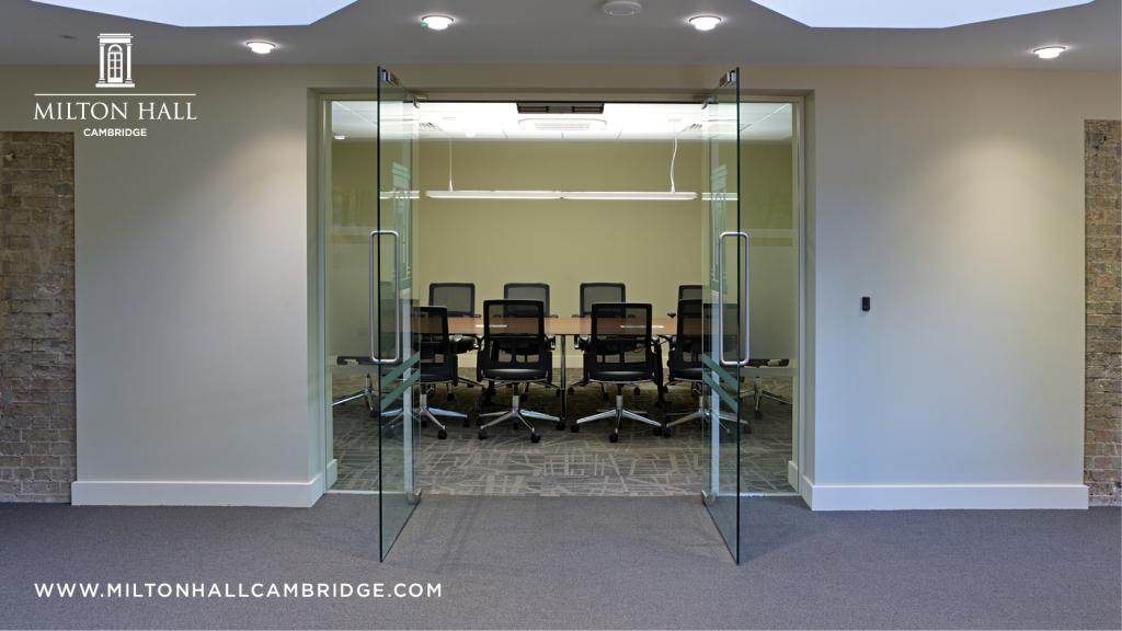Photo shows glass doors open on a room set up for a meeting with chairs around a rectangular table. 