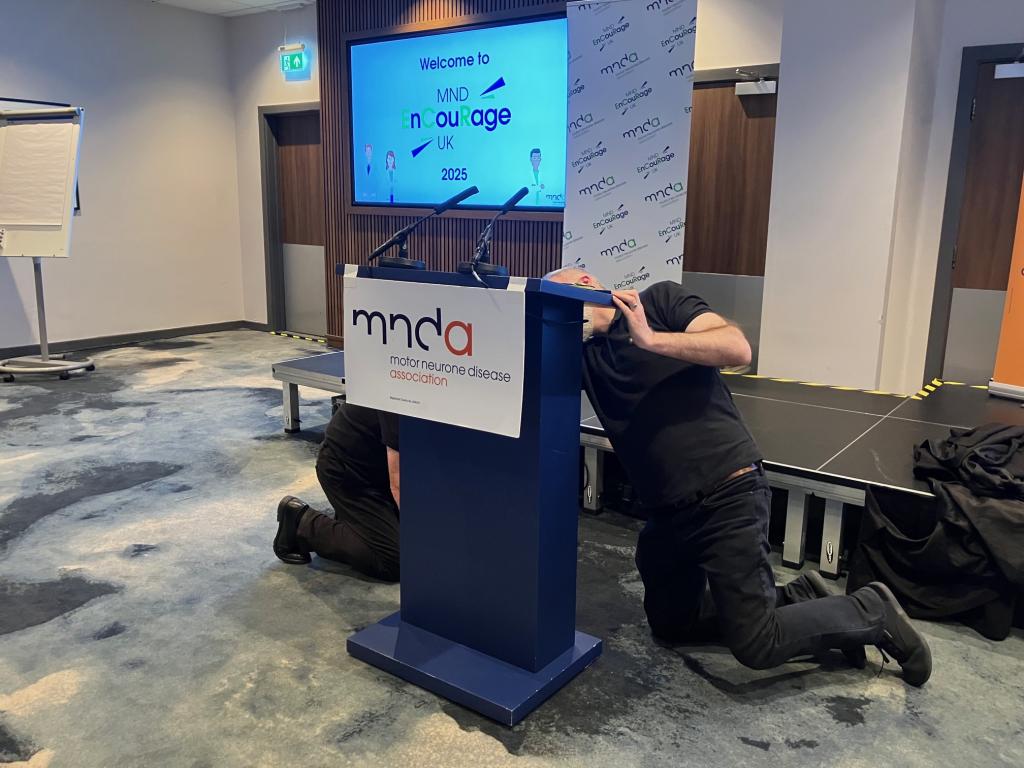 Two men moving a lectern at the front of a conference hall