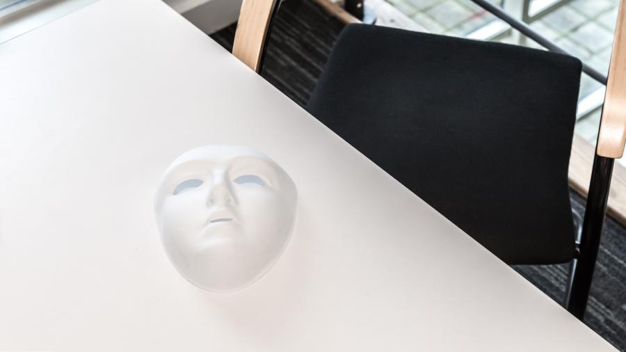 White mask on a white table with dark chair in the background
