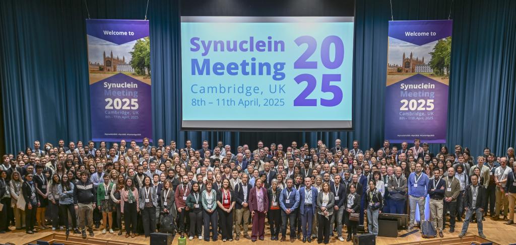 A diverse group of professional people on the stage at West Road Concert Hall Cambridge for the Alpha Synuclein Conference. Photo Credit: AS2025