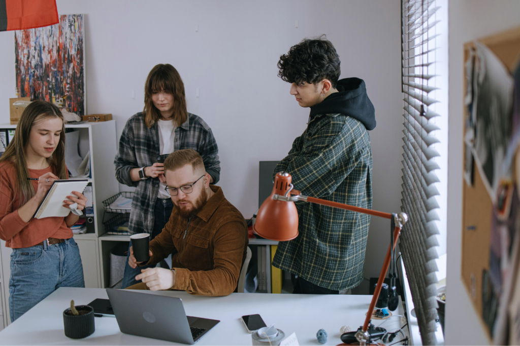 A group of young people chatting to each other around a person working at a laptop