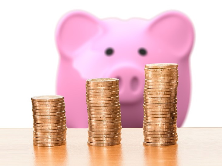 A pink piggy bank sits behind three piles of coins.