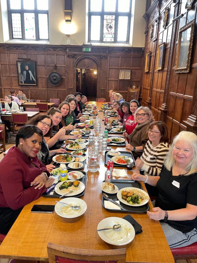 A mixed group of people eating at a long wooden table in a Cambridge College