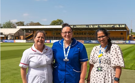 three nurses stand, smiling, in front of the cledara abbey stadium on a sunny day 