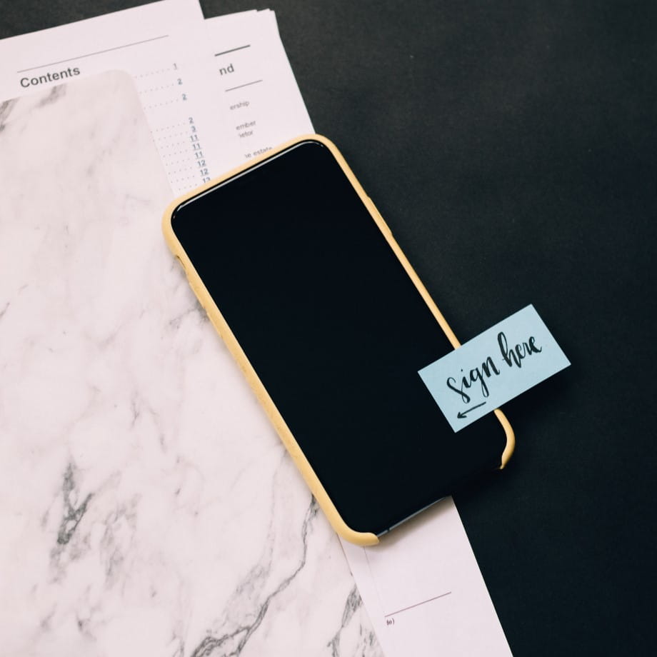 A mobile phone with a written note on it saying sign here.