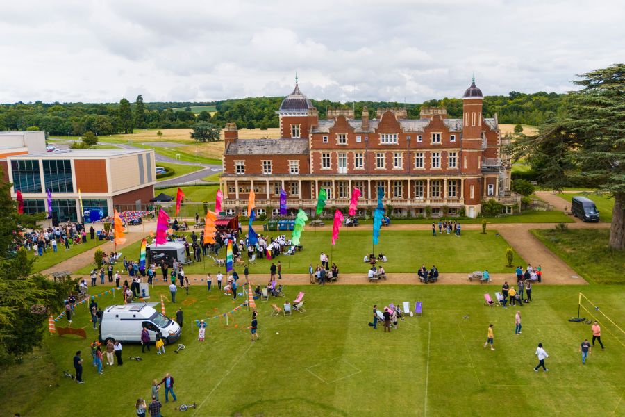 Photo of a festival event on the back lawn at Babraham Research Campus. There are people playing outdoor games, festival flags and food trucks. 