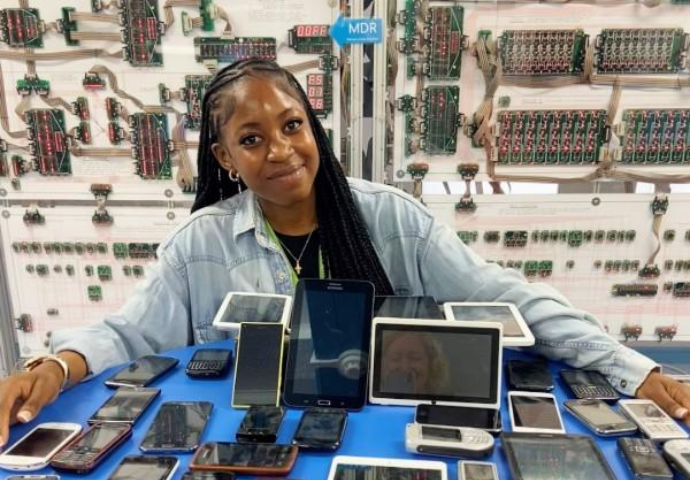 Smiling young woman with a table of outdated technology including mobile phones and tablets