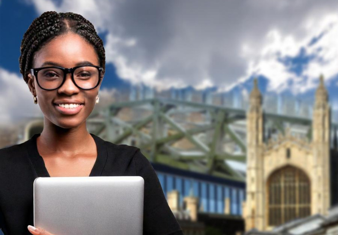 A smiling lady standing with a laptop. The bridge of sighs, Kings college and the Fitzwilliam Museum are in the background