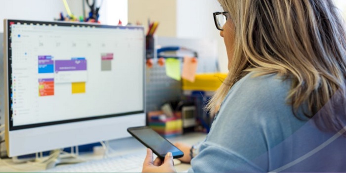 Woman looking at  mobile phone and calendar on her computer screen