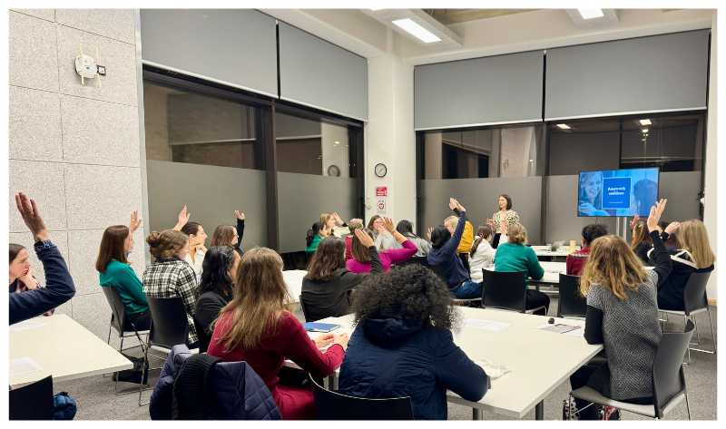 A room of people around tables raising their hands to a question