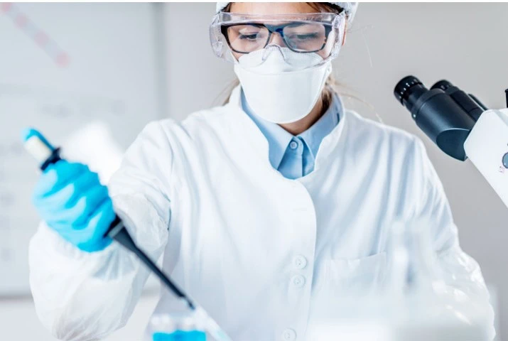 A person in a lab coat and goggles holding a pipette AI-generated content may be incorrect.