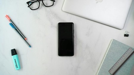  A phone, laptop and notebook on a desk. 