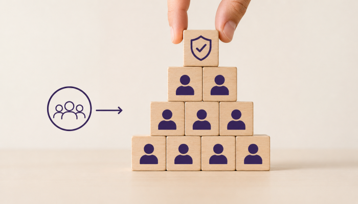 Hand placing a structured block onto a team pyramid, representing how growing companies protect culture by turning values into repeatable hiring processes.