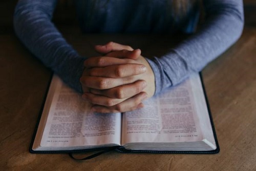 man with hands together over an open book
