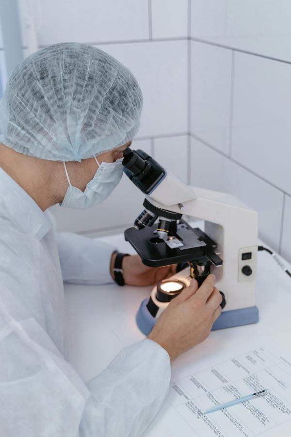 Scientist looking down through a microscope and reviewing data on a chart. 