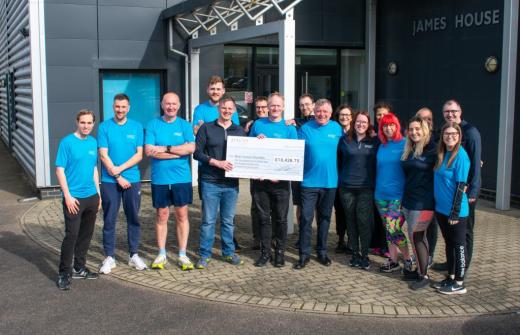 an image of several Pico Technology employees wearing running tops outside the headoffice and holding a large foamboard cheque