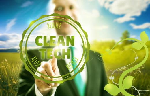 Man with blue sky and green grass behind him, pressing a Clean Tech button on the screen in front of him - promoting the green business concept.