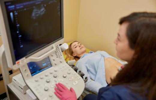 A gynecologist is performing an early pregnancy ultrasound screening, for a young female lying on a medical bed.