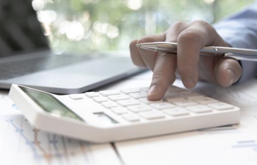Accountant's hand on a calculator ,with laptop alongside, calculating income expenditure and investment data