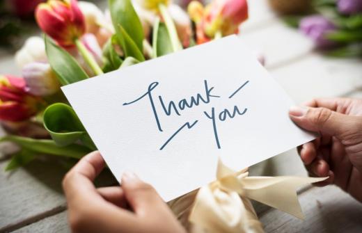 tulips on a table with a feminine hand holding a white card that says Thank You written on it