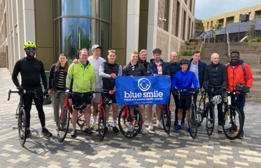 Group of people with bikes holding up a 'Blue Smile' banner outside a building